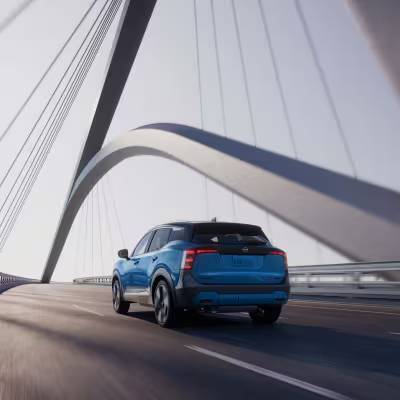 A blue 2026 Nissan Kicks drives over a suspension bridge