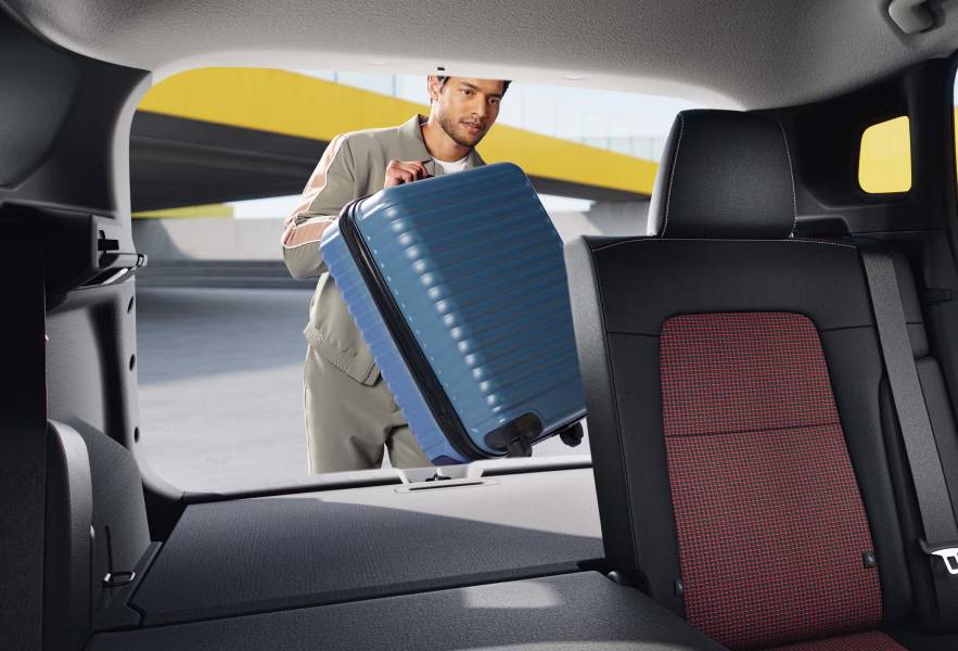 A man loads a blue suitcase into the cargo space of the 2026 Nissan Kicks with the back row folded 60/40