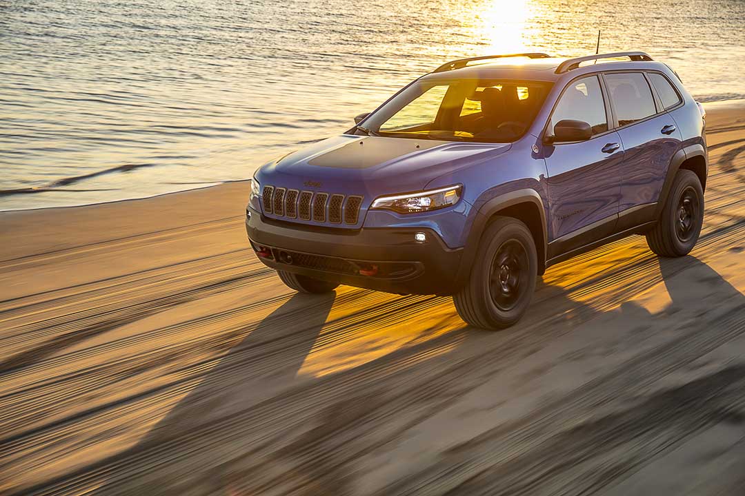 Le VUS Jeep Cherokee Trailhawk 2021 bleu roulant sur une plage au bord de la mer