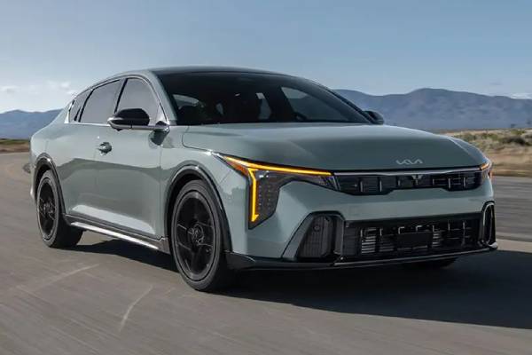 The front profile of a blue 2026 Kia K4 Sedan as it drives along a highway.