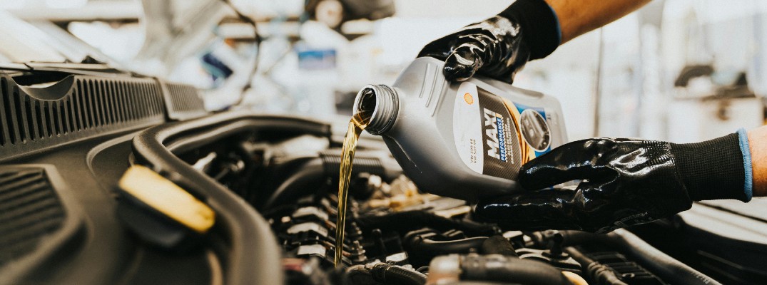 A stock photo of a person adding fresh oil to a car's engine.