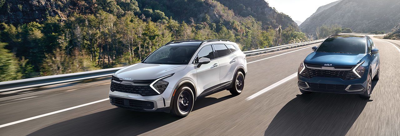 Front side view of two Sportage models with tree-covered hills in the background