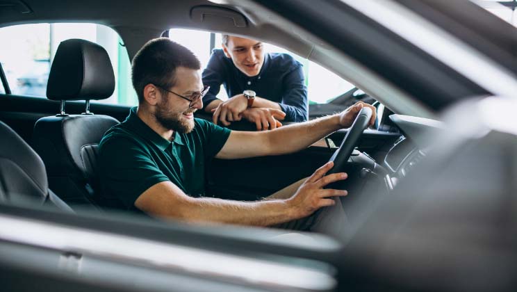 Person in car testing it with sales associate looking on from outside