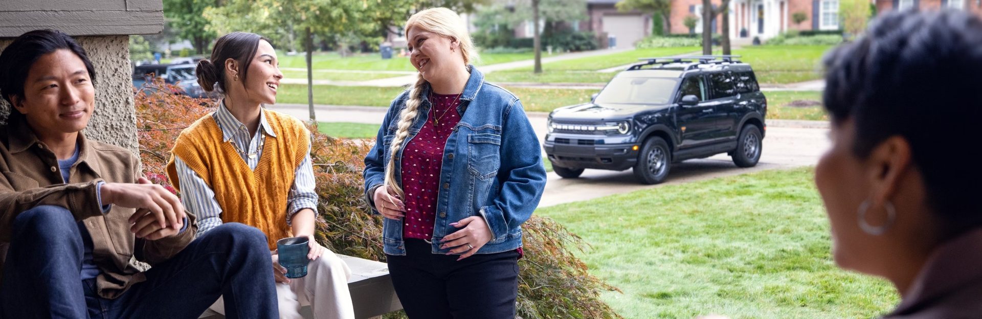 Unknown people sitting and chatting outdoors with Bronco parked nearby