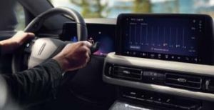 Hands_over_steering_wheel_of_lincoln_model_interior_with_dash_and_screen_display