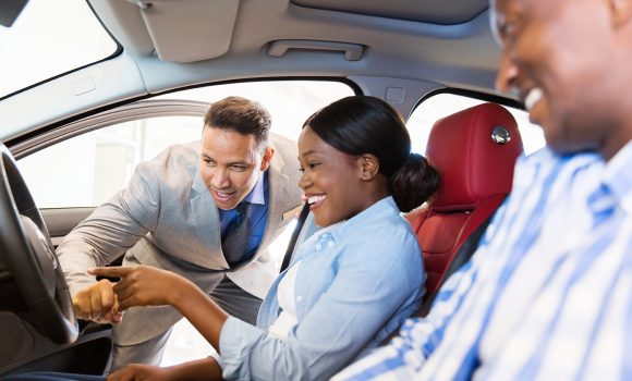 salesman showing new car to african couple in showroom