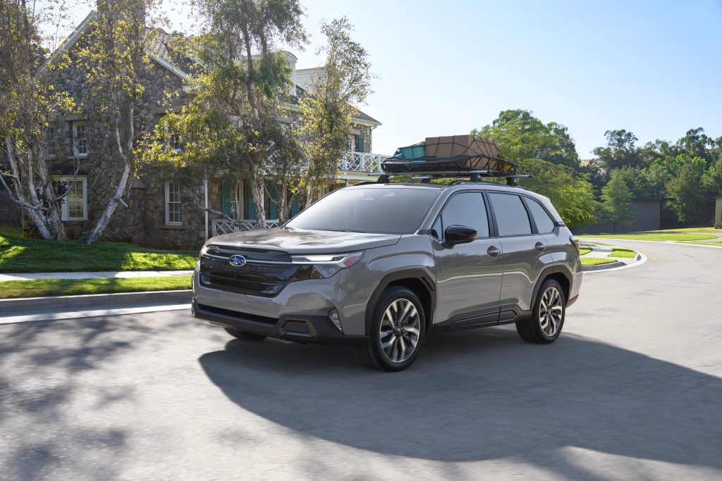 2026 Subaru Forester driving through a residential neighbourhood with a roof rack loaded with camping and cargo gear.