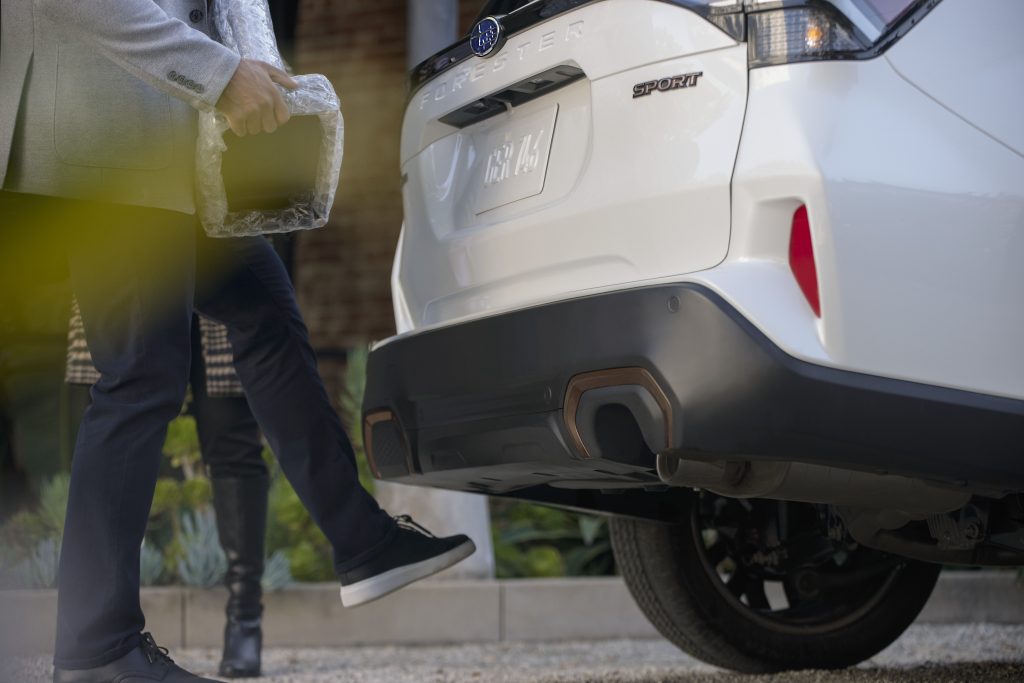 Person activating the 2026 Subaru Forester Sport hands-free power liftgate by kicking under the rear bumper while carrying a package.