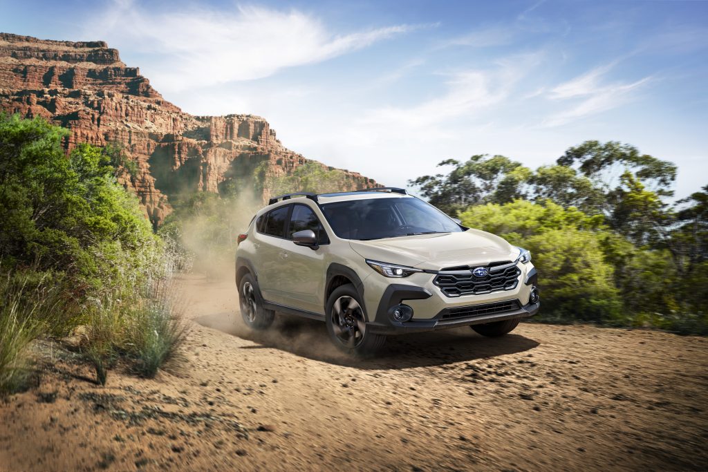 2026 Subaru Crosstrek driving on a dirt trail with dust behind it, surrounded by trees and rocky cliffs, highlighting its off-road performance.