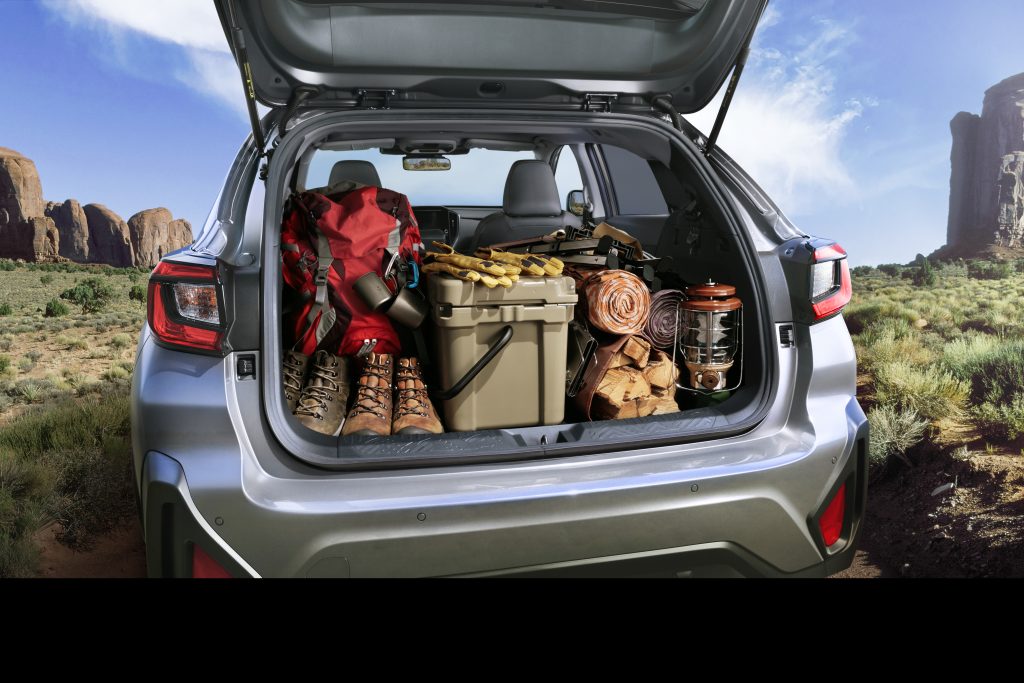 Rear view of the 2026 Subaru Crosstrek with the hatch open, showing a fully packed cargo area filled with hiking boots, backpack, cooler, firewood, and camping gear in a desert landscape.
