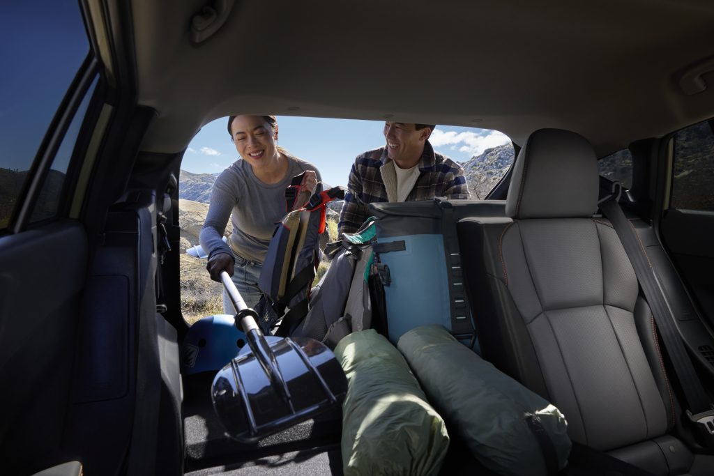 View from inside the 2026 Subaru Crosstrek cargo area with two people loading camping gear, backpacks, and a shovel through the open hatch.