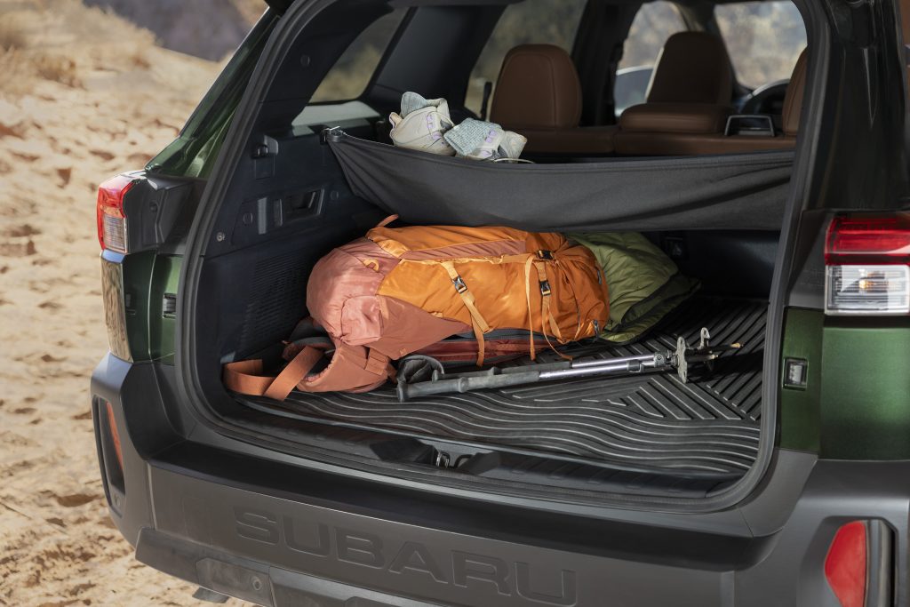 Open rear hatch of a 2026 Subaru Outback showing rubber cargo mat, hiking backpack, sleeping bag and trekking poles loaded in the cargo area.