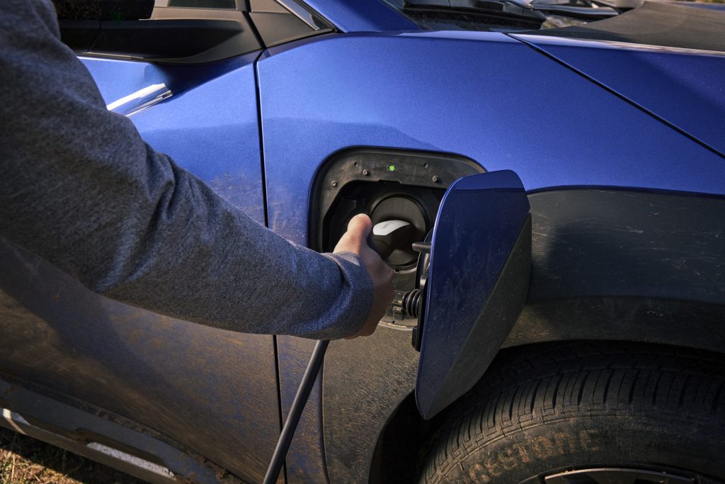 Close‑up of a person plugging a charging cable into the charge port of a blue 2026 Subaru Trailseeker electric SUV.