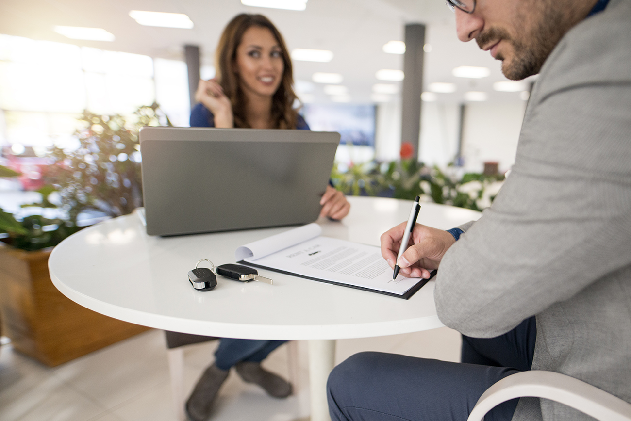 Car buyer signing a contract in vehicle dealership. Buying a new car. Car keys on the table.