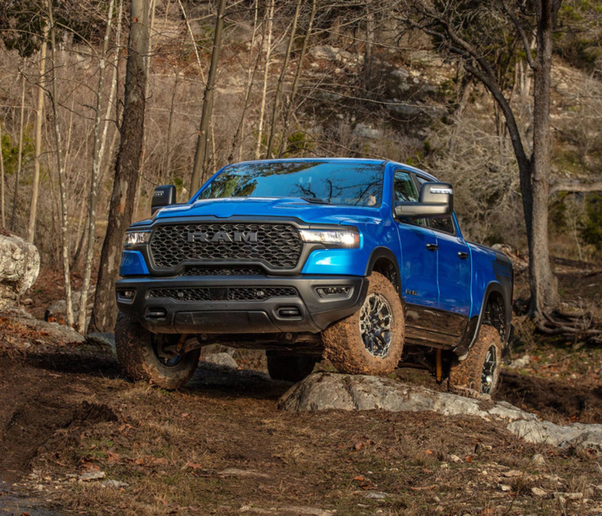 A blue 2025 Ram 1500 sits on stony offroad track with trees in the background