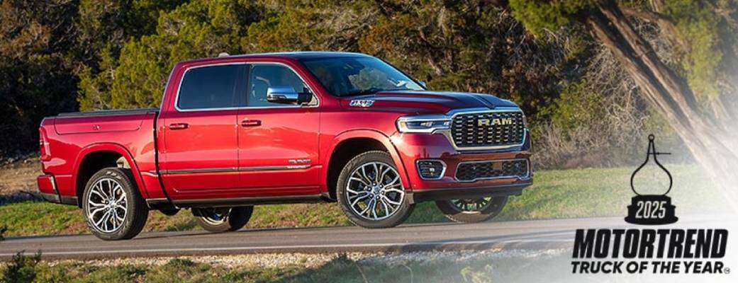 A red 2025 Ram 1500 sits on a grassy verge. In the corner, black text says "MotorTrend 2025 Truck of the Year"