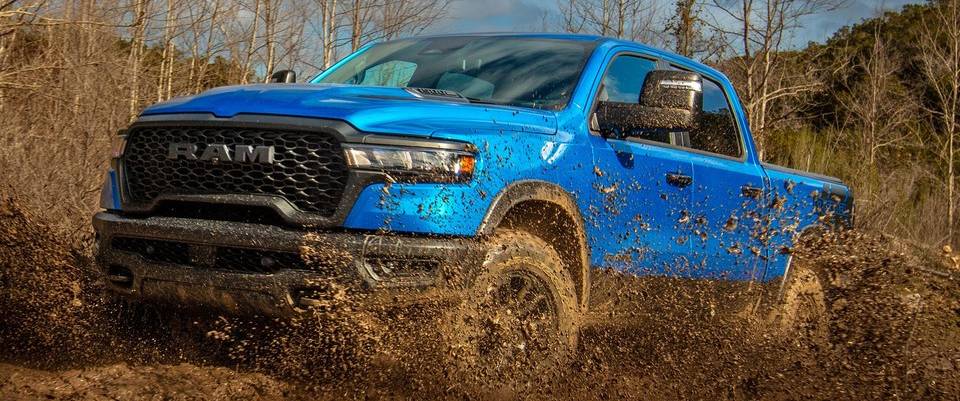 A blue 2026 Ram 1500 kicks up mud off-road