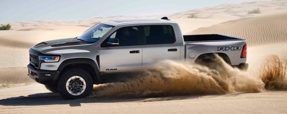 A silver 2026 Ram 1500 RHO speeds across the desert, kicking up sand