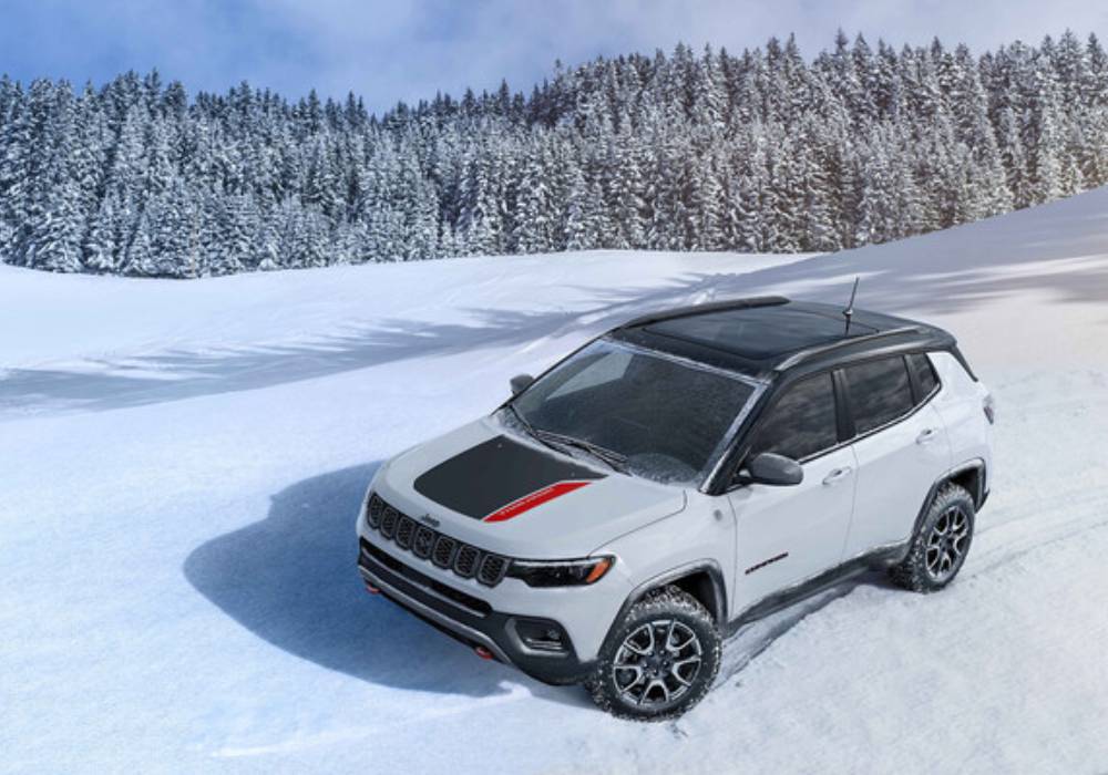 A white 2026 Jeep Compass with a black and red hood decal drives over snow