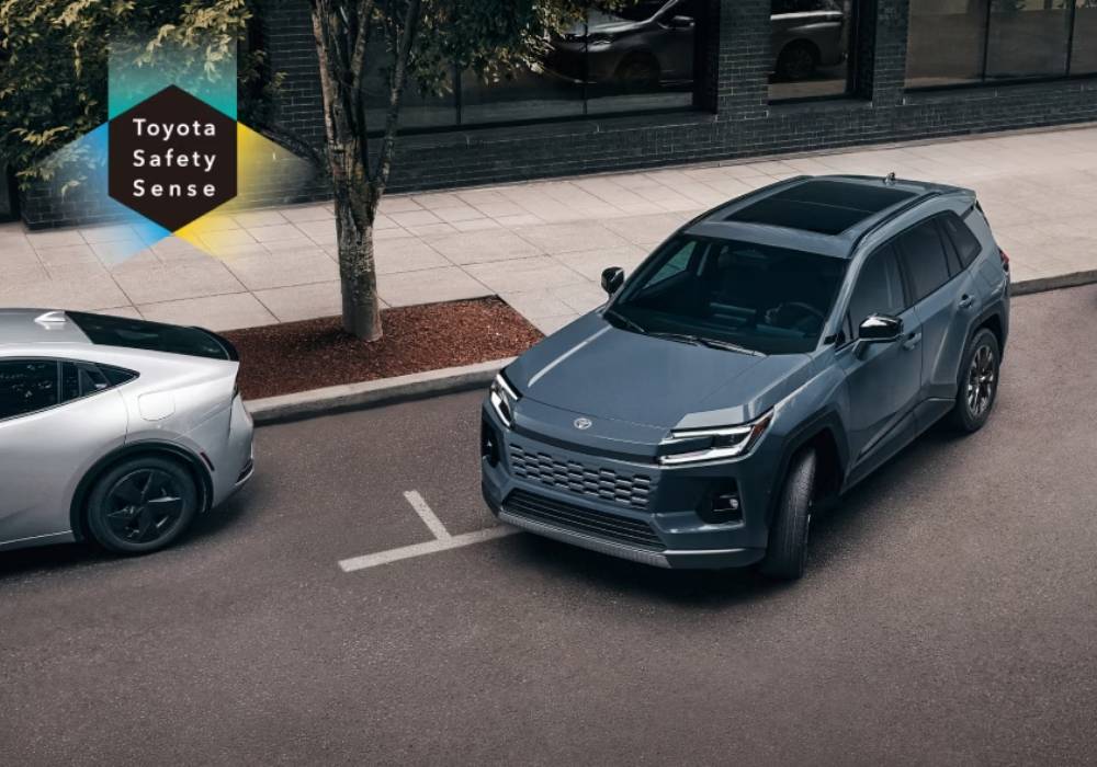 A blue Toyota vehicle pulls away from the curb in a city. The Toyota Safety Sense logo is shown in the top left