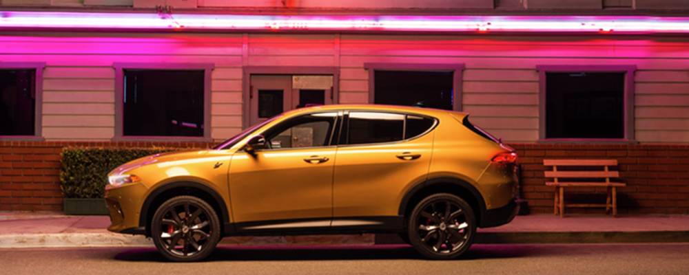 A yellow 2025 Dodge Hornet is parked in front of a building with pink neon lights. 2026 Dodge Hornet design features at Tarrabain Motor Products in Lac La Biche, AB