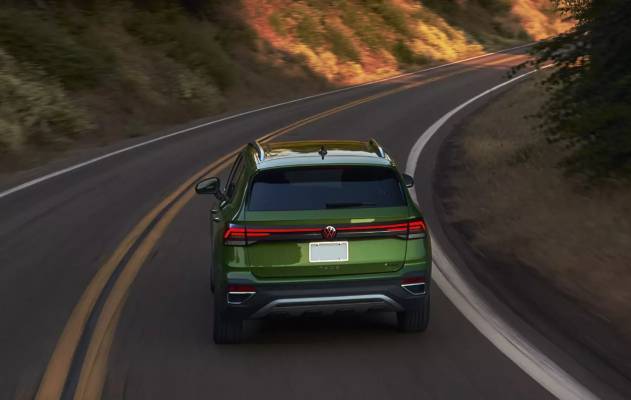 A green 2025 Volkswagen Taos drives on a road that curves past a rugged cliff wall