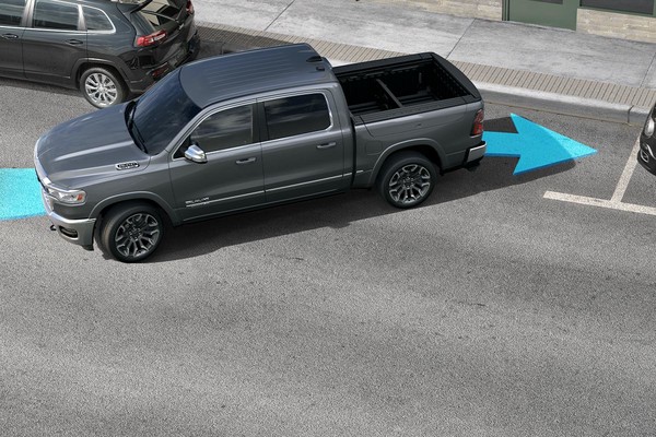 2026 Ram 1500 Park-Sense® Automated Parking System. A silver 2026 Ram 1500 reverses into a parking spot with a blue arrow to telegraph its direction