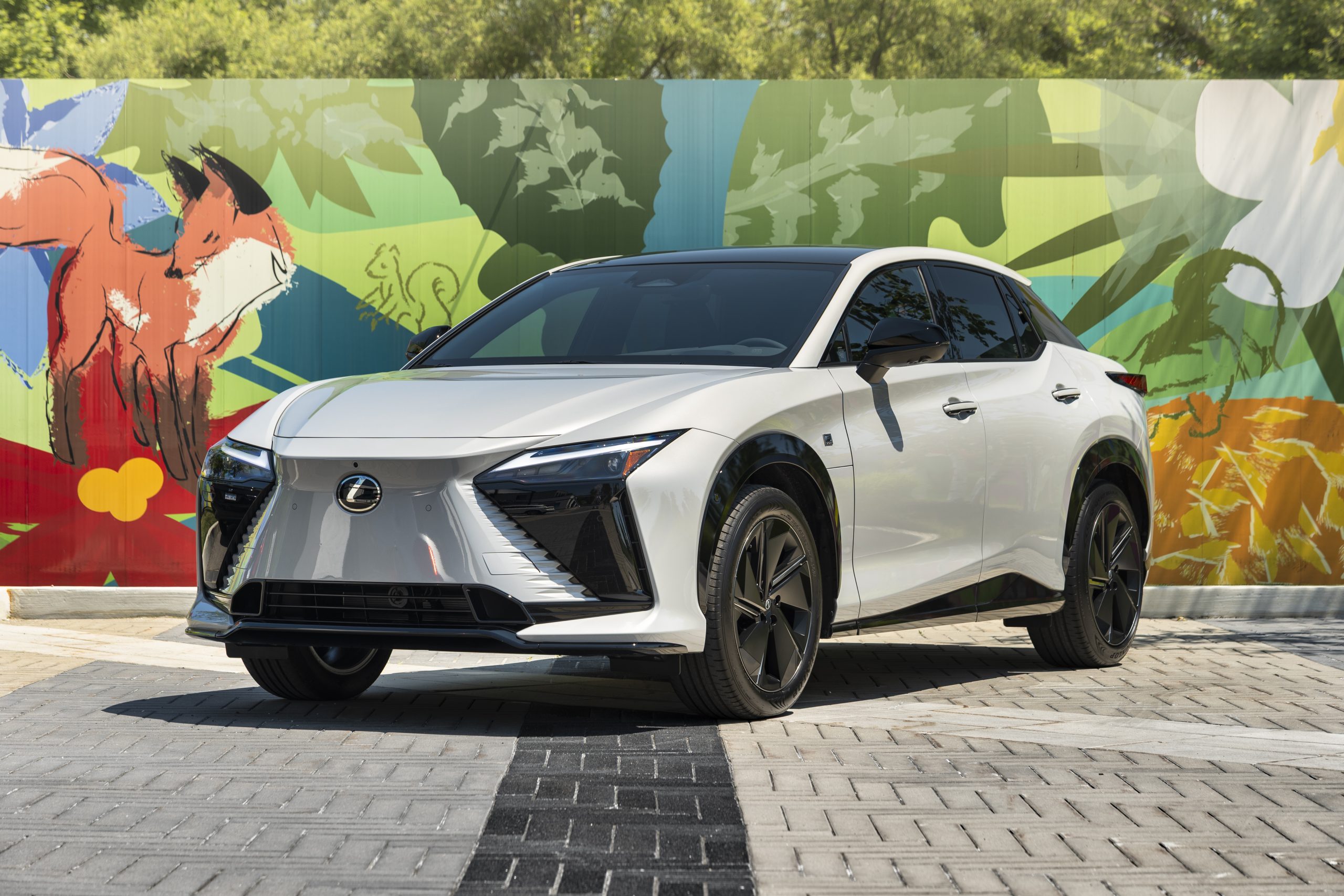 2026 Lexus RZ 550e F SPORT AWD in white parked in front of a colourful outdoor mural featuring a fox and nature elements.