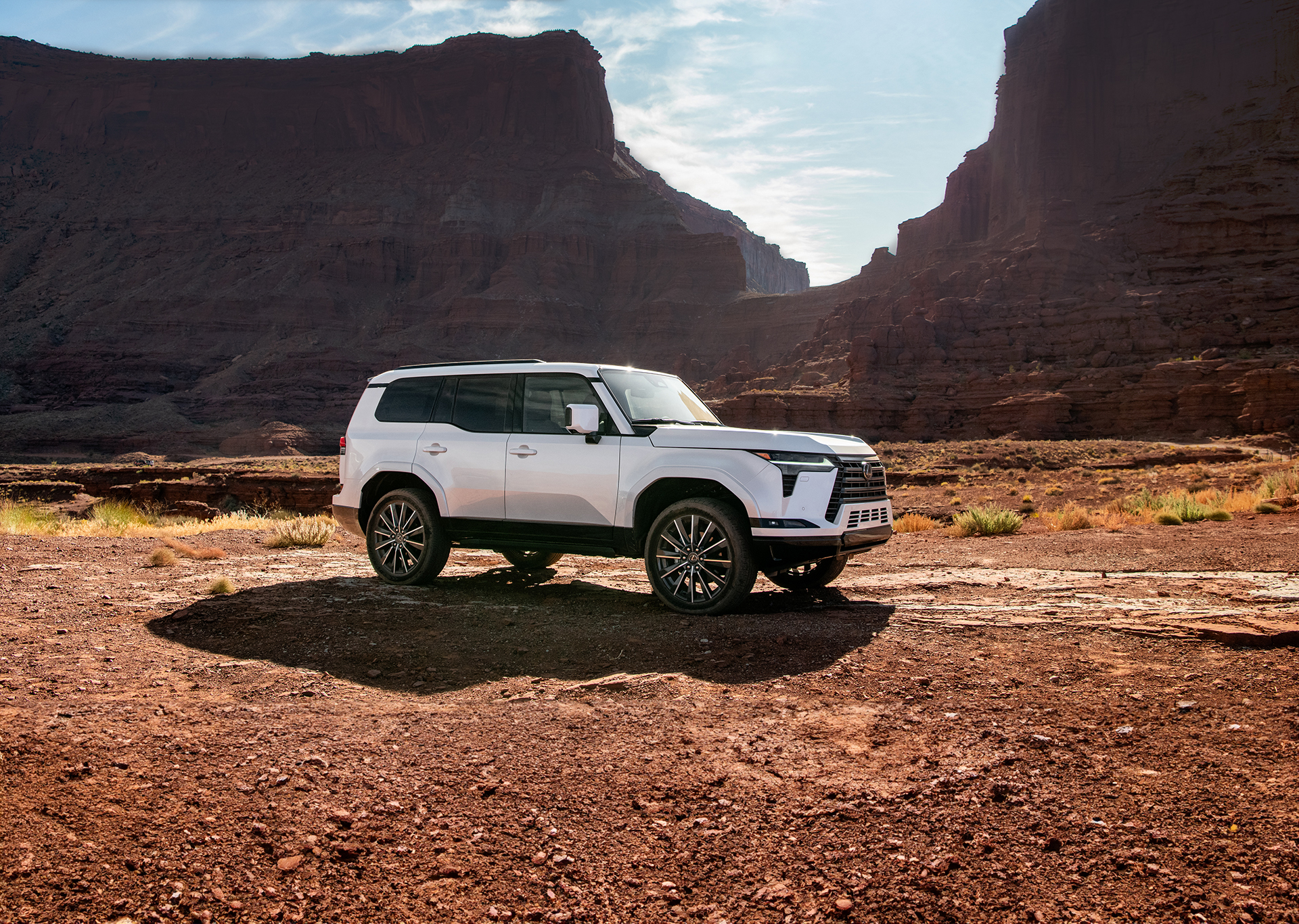 2026 Lexus GX 550 Executive in Eminent White Pearl parked in a desert canyon landscape, showcasing its bold design, high ground clearance, and rugged capability.