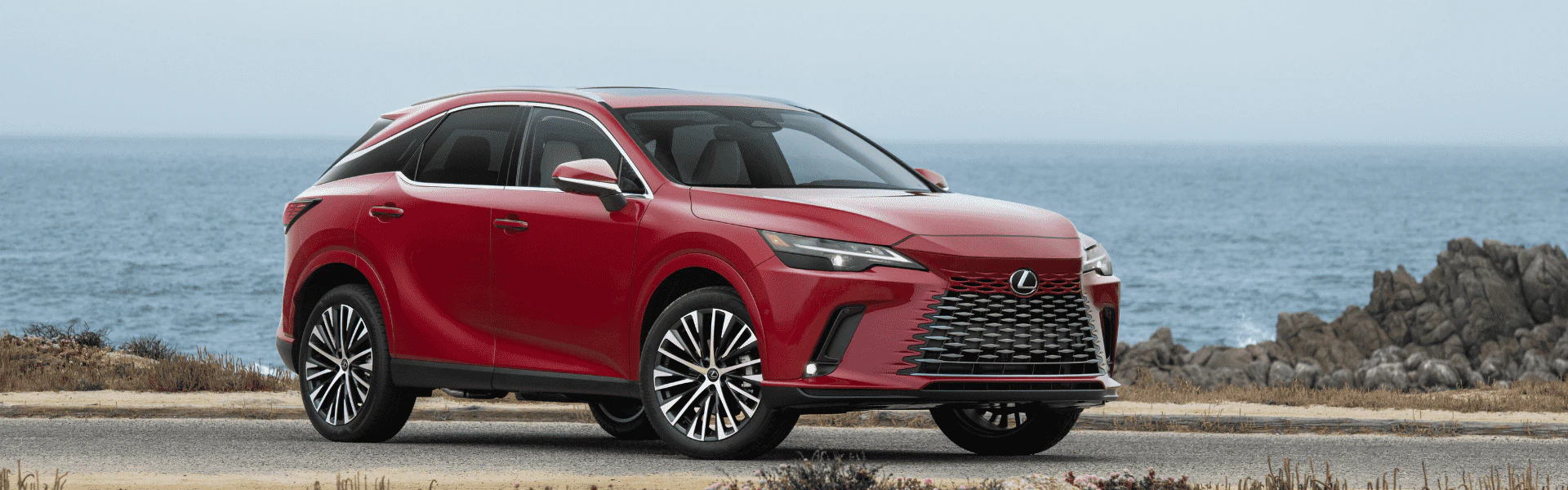Red 2026 Lexus RX 350h parked on a coastal road with ocean in background