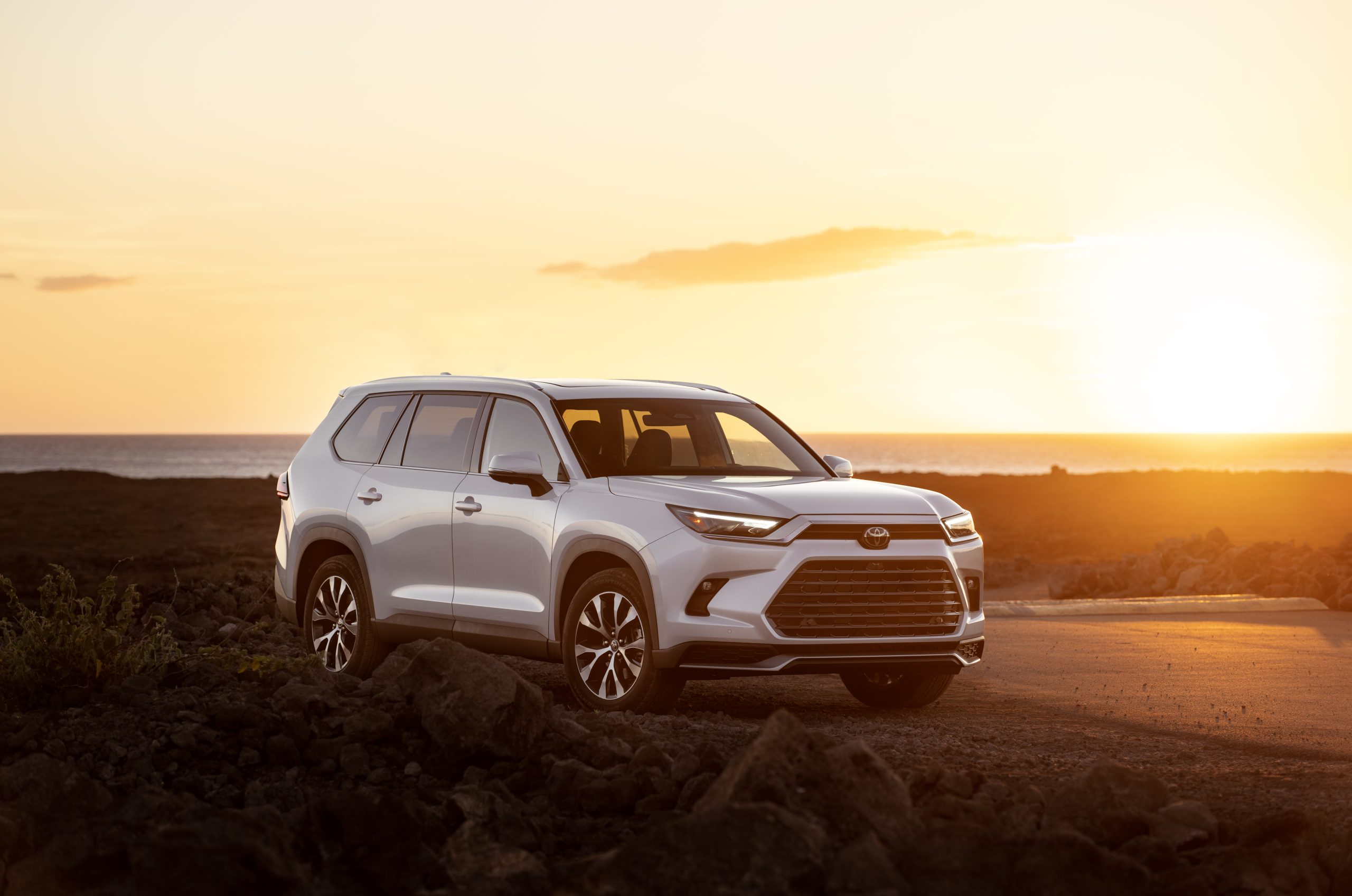 2026 Toyota Grand Highlander in white parked at sunset near the ocean.