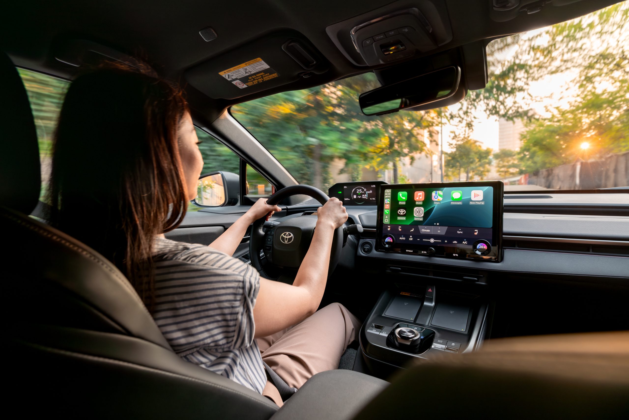 A woman driving a Toyota vehicle with a modern digital dashboard and a large touchscreen infotainment system displaying Apple CarPlay apps.