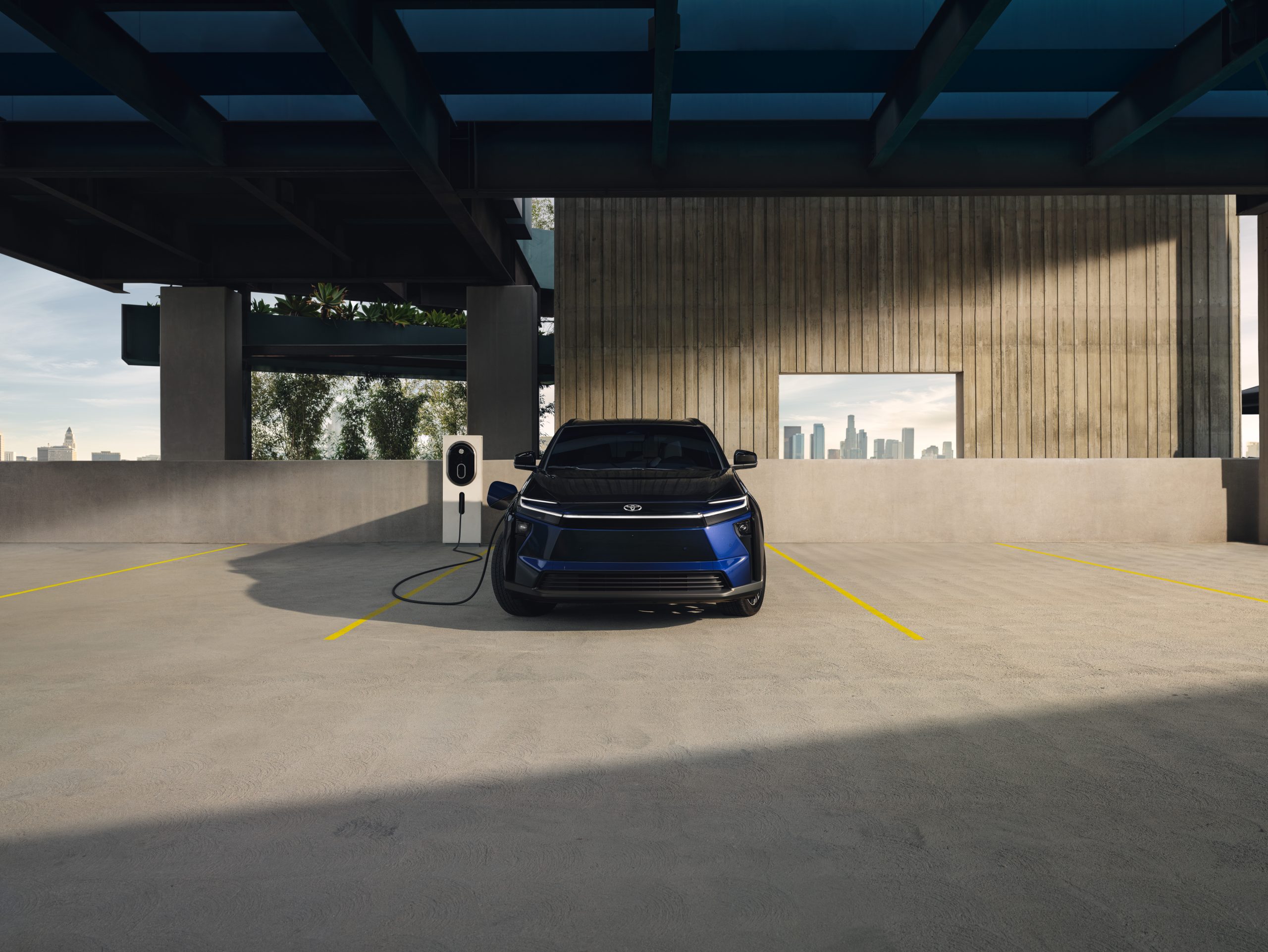2026 Toyota bZ electric SUV charging at a public charging station in an open-air parking structure.