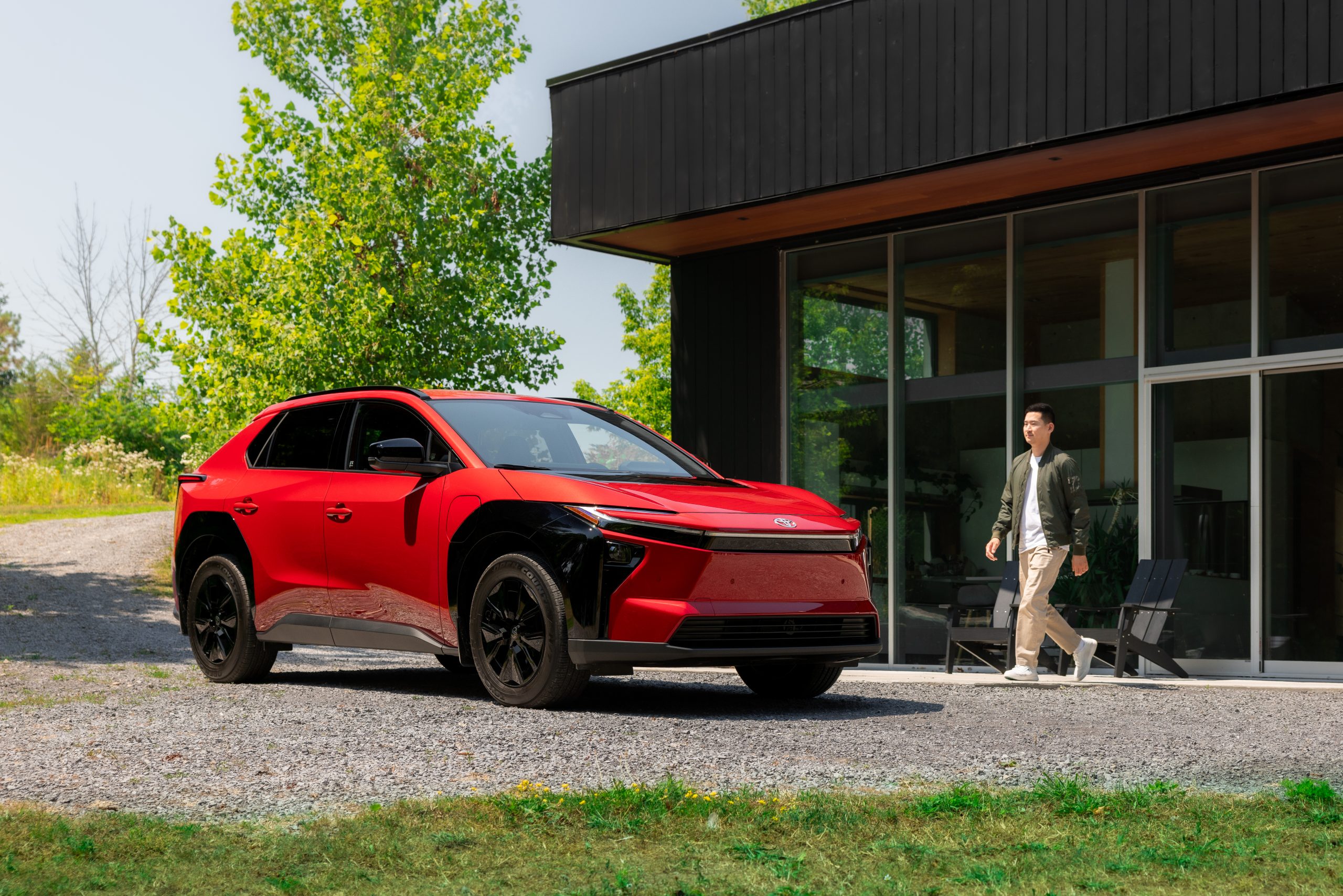 Red 2026 Toyota bZ electric SUV parked outside a modern home with a person walking nearby.