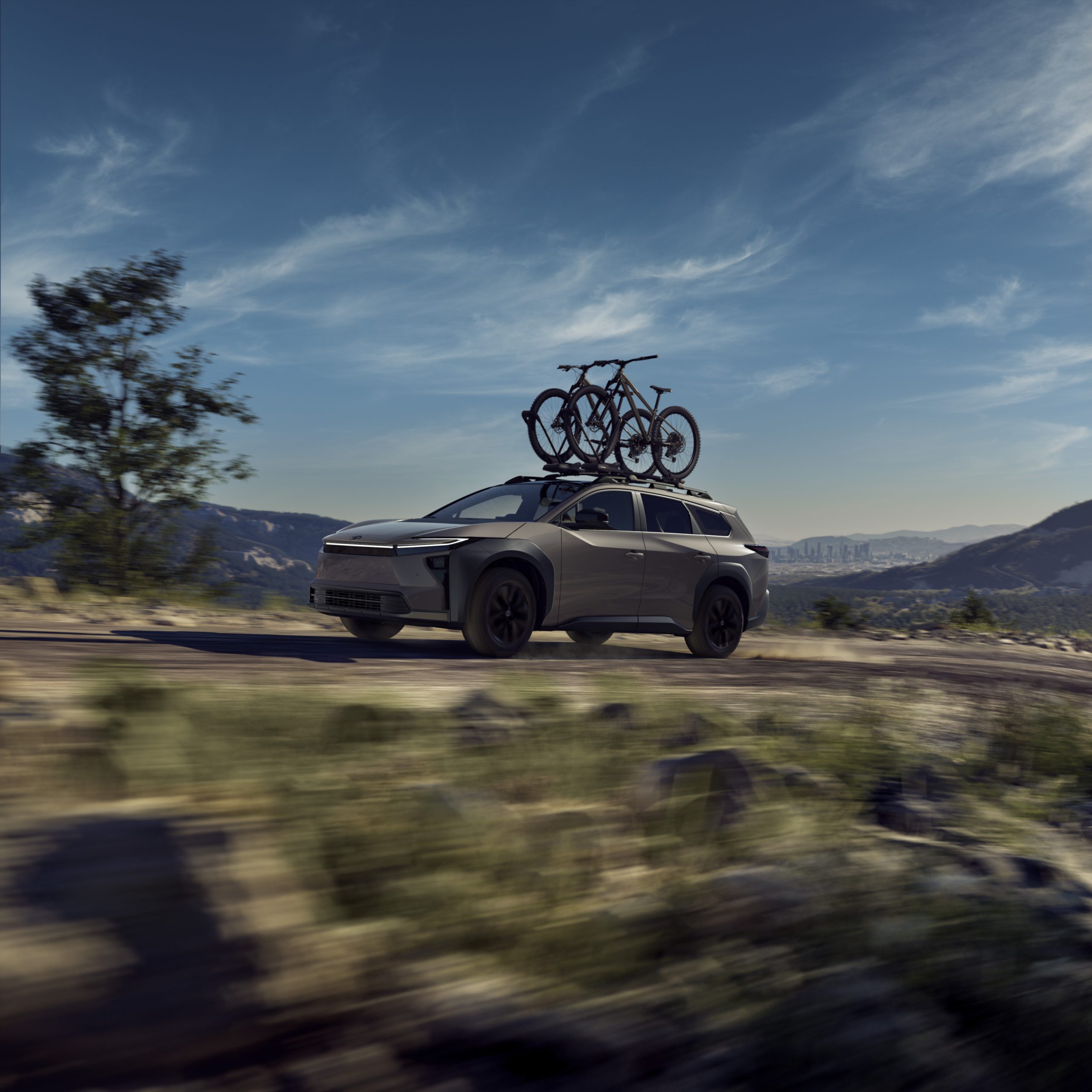 2026 Toyota bZ Woodland Edition SUV driving on a scenic trail with mountain bikes mounted on the roof.