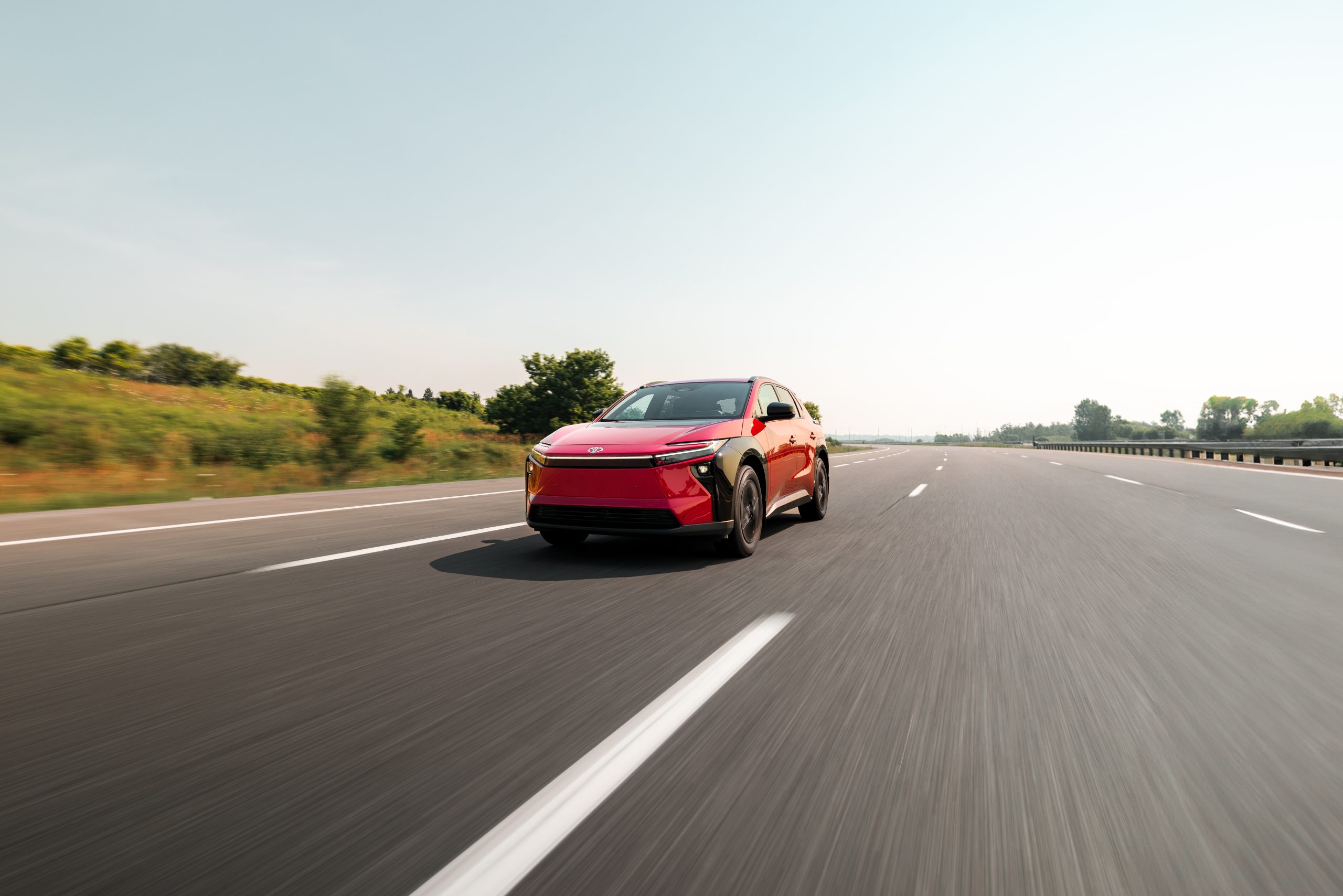 Red 2026 Toyota bZ driving on an open highway under clear skies, showcasing its sleek aerodynamic design and electric performance.