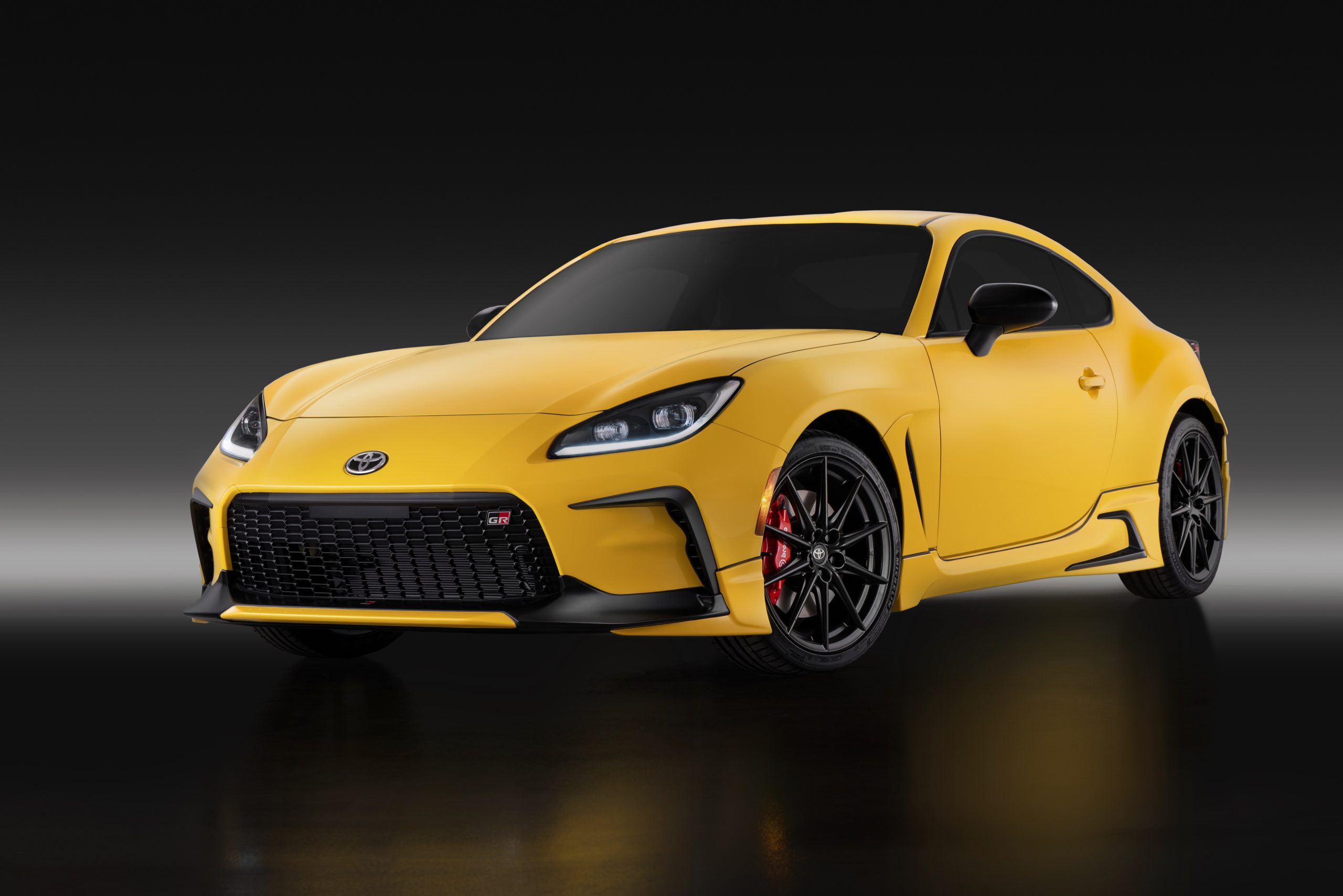 Front three-quarter view of the 2026 Toyota GR86 Yuzu Edition in bright yellow, featuring black aerodynamic accents, matte black wheels, and red Brembo brakes.