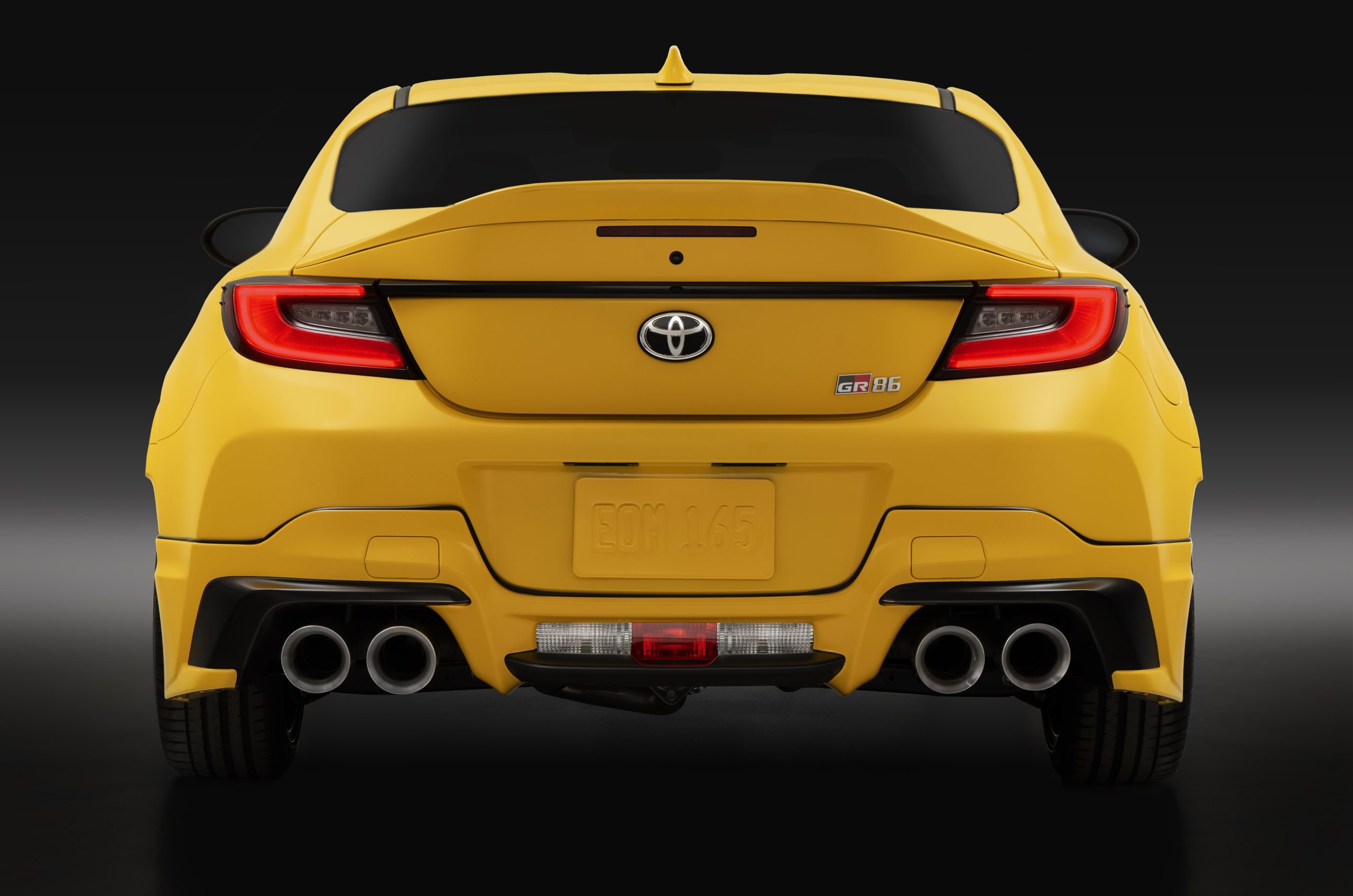 Rear view of the 2026 Toyota GR86 Yuzu Edition in yellow, showcasing its quad exhaust tips, GR86 badge, and aerodynamic rear spoiler.