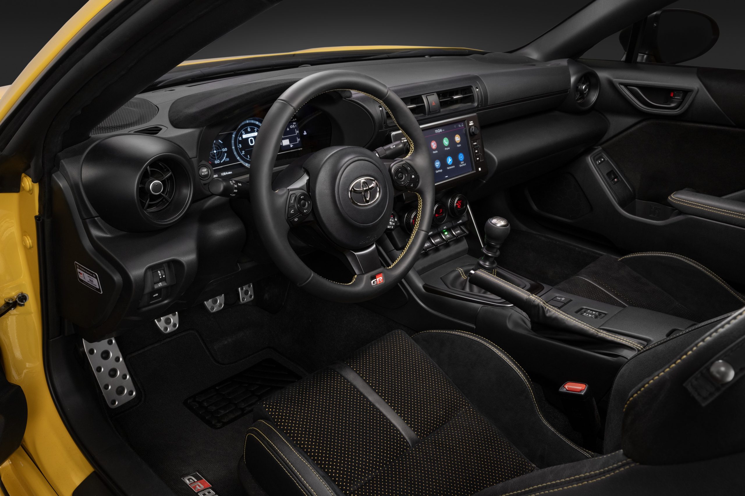 Interior of the 2026 Toyota GR86 Yuzu Edition showing the driver-focused cockpit, sport seats with yellow stitching, and manual transmission.
