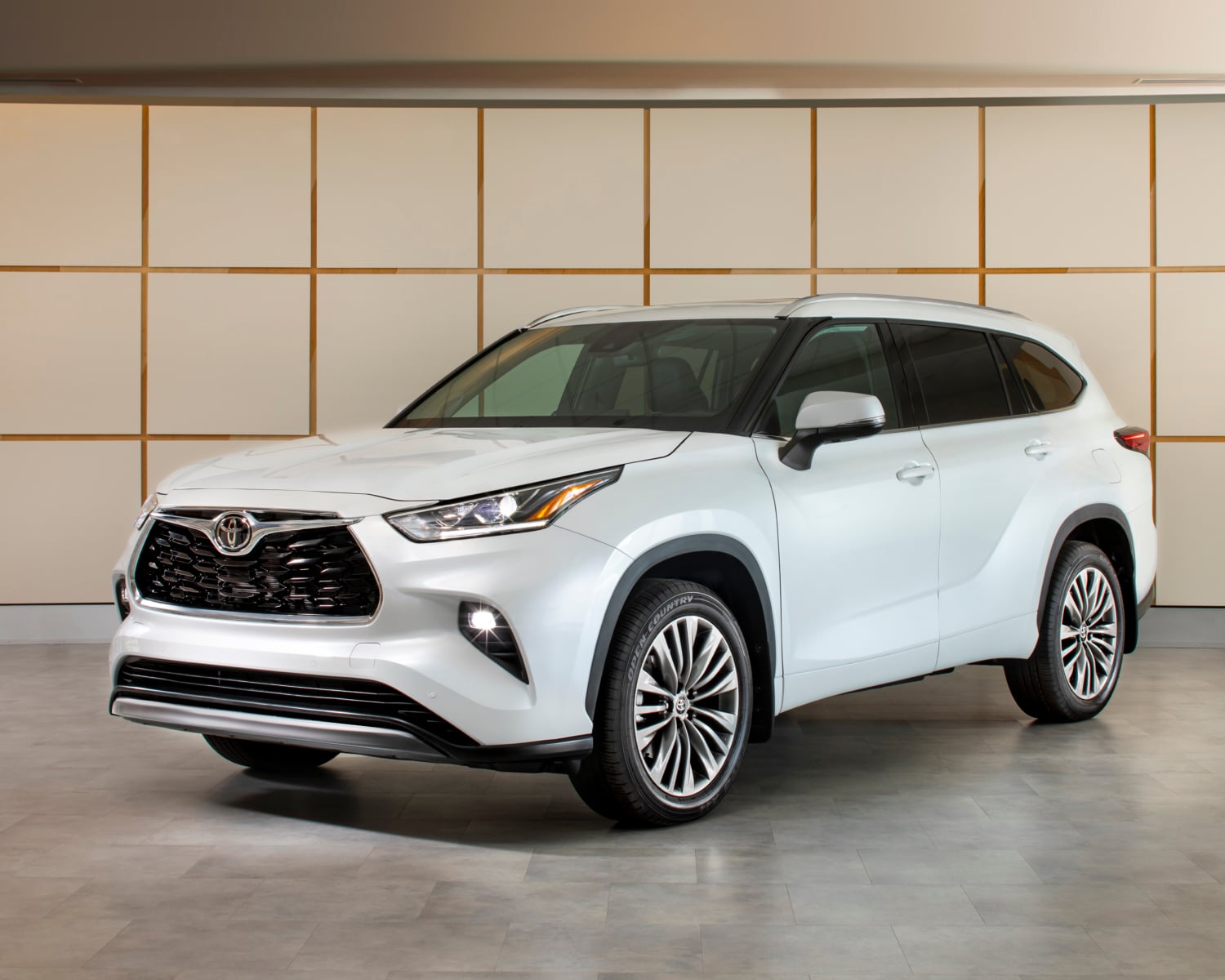2026 Toyota Highlander Limited Platinum in Wind Chill Pearl parked indoors showcasing its bold front grille and sculpted SUV design.