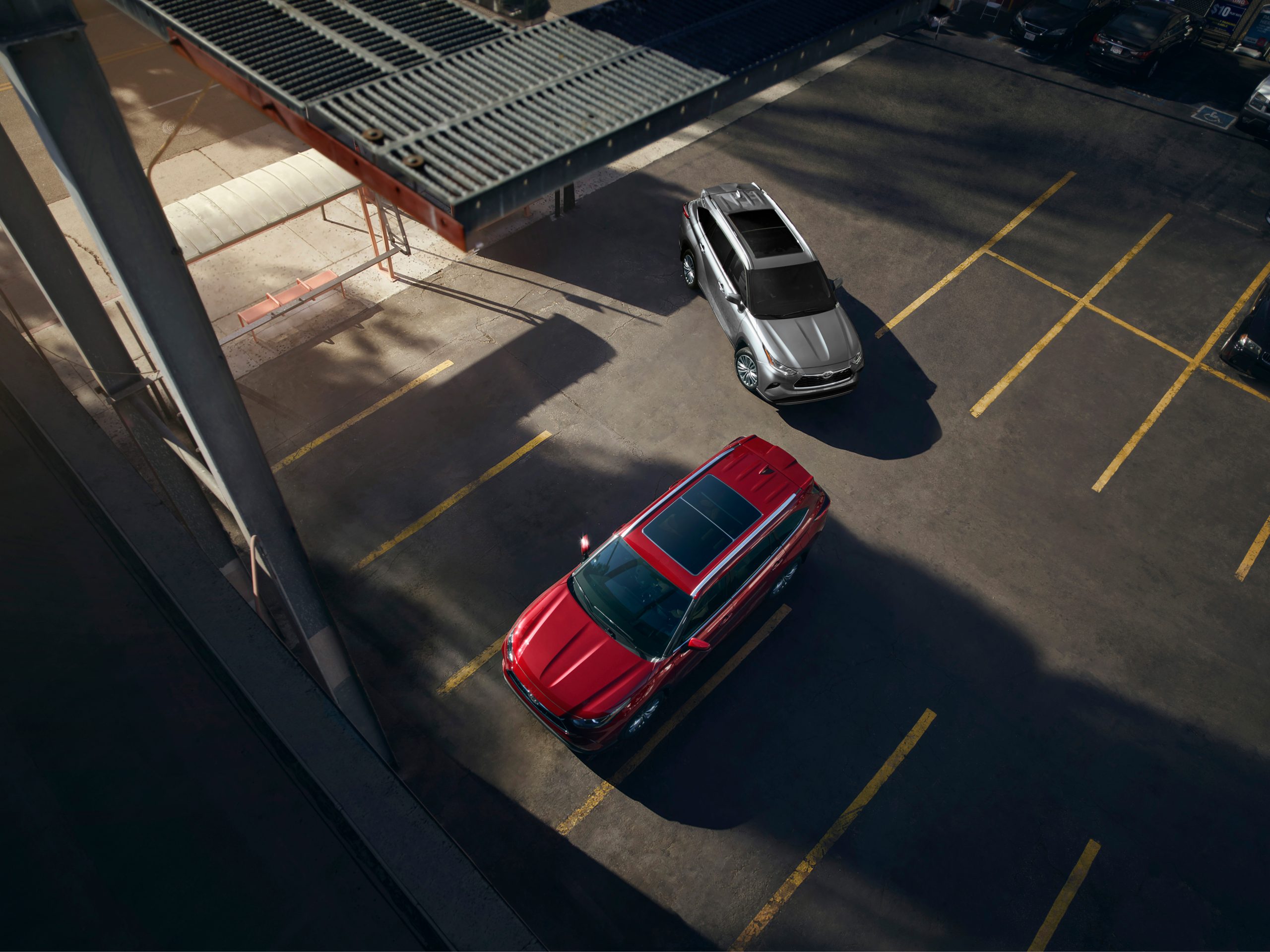 2026 Toyota Highlander Hybrid Platinum models in Heavy Metal and Ruby Flare Pearl parked outdoors, showcasing bold color options and premium design.