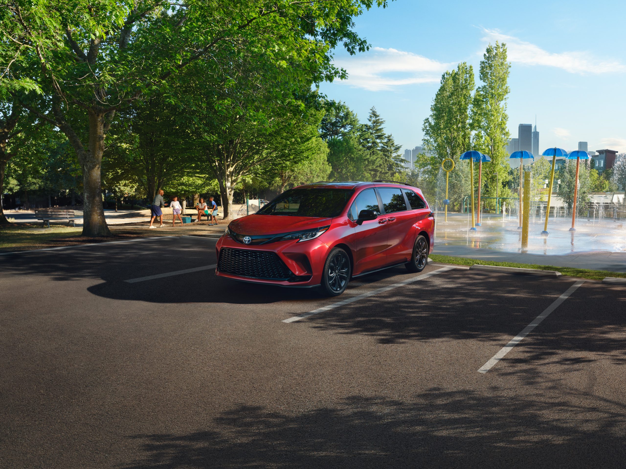 Front three-quarter view of a red 2026 Toyota Sienna XSE FWD parked near a splash pad in a park.