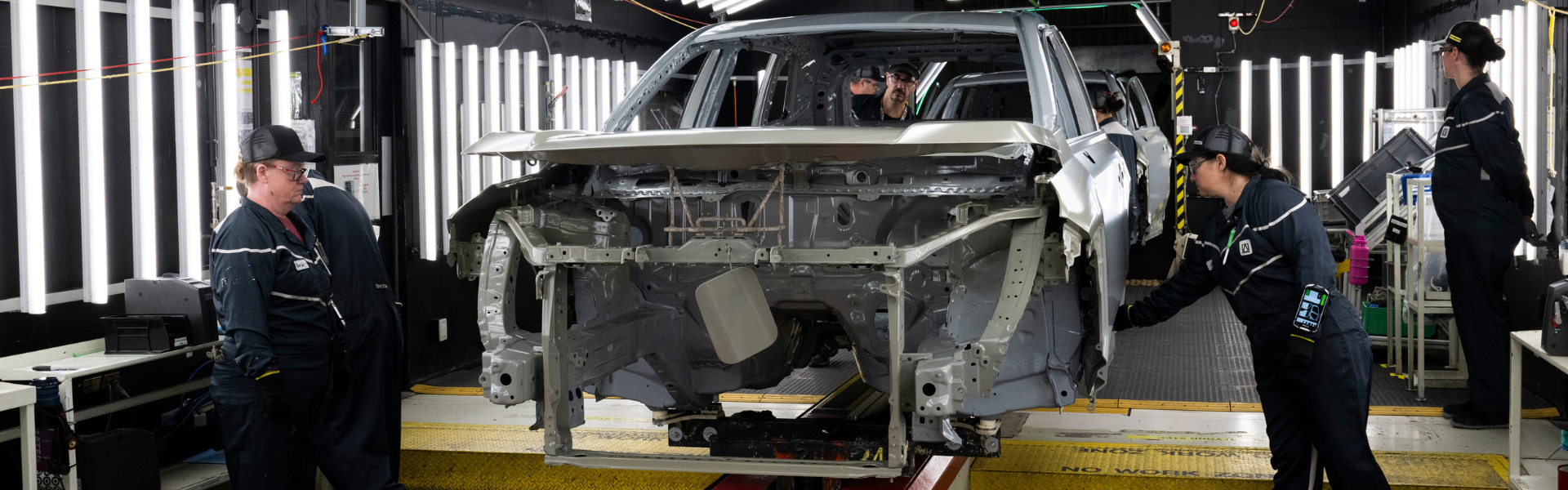 Toyota vehicle body frame on factory assembly line with workers inspecting components