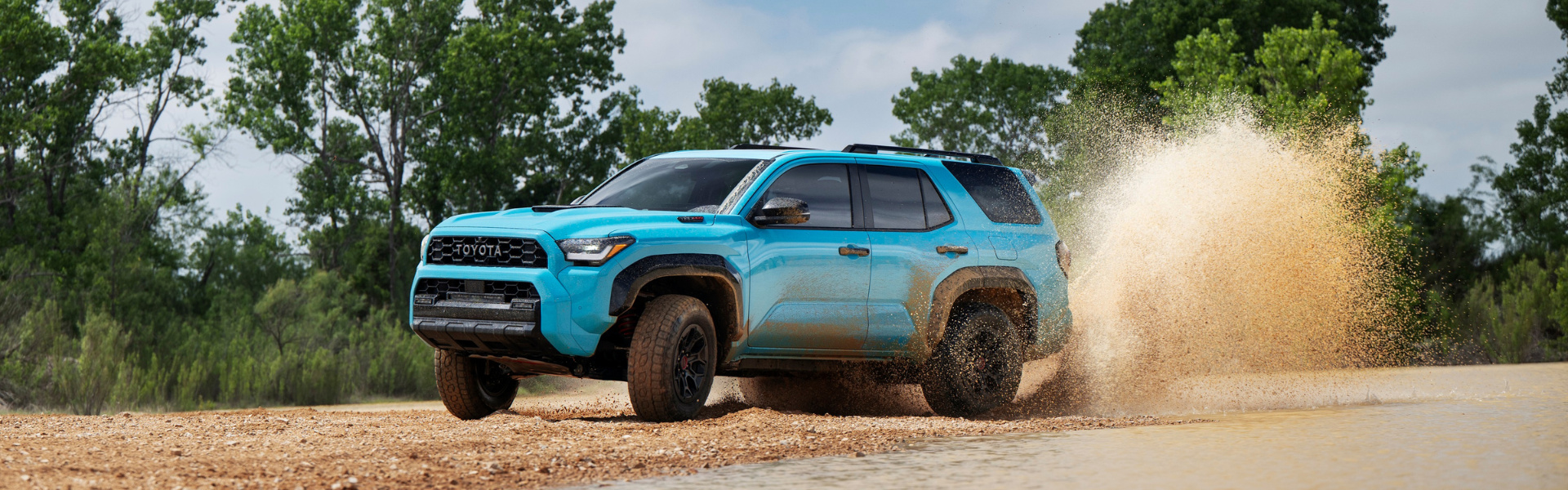 Blue Toyota 4Runner driving through shallow water on a dirt trail