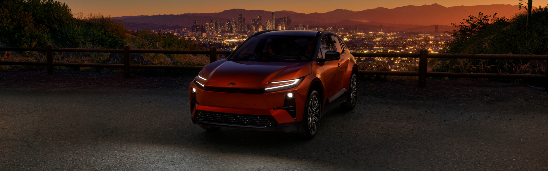 Red Toyota C-HR parked at a scenic overlook with city skyline illuminated at night