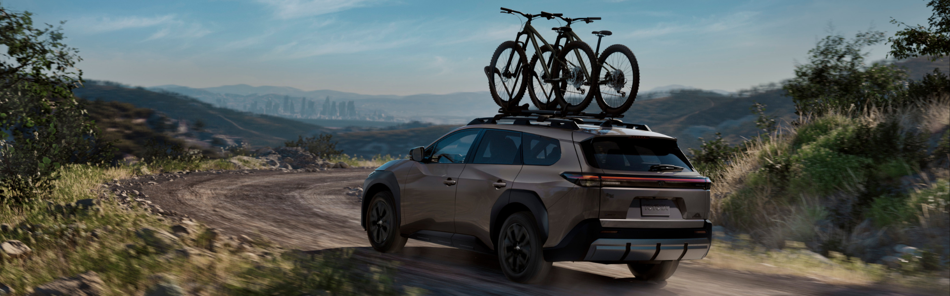 Toyota bZ driving on a dirt road with two bicycles mounted on a roof rack