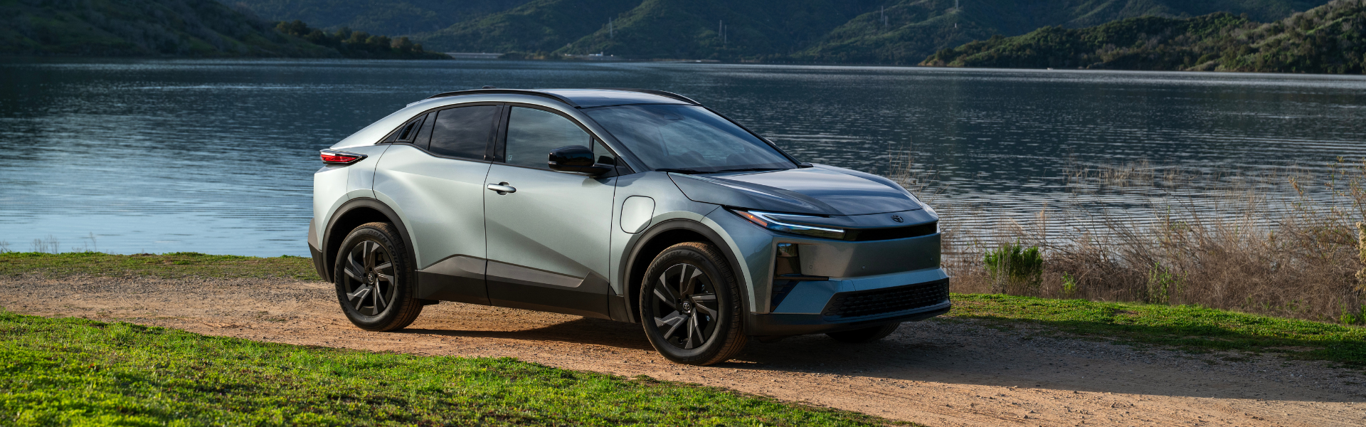 2026 Toyota C-HR parked on a dirt road beside a lake with hills in the background