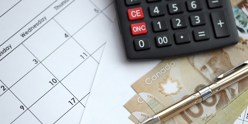 A calculator, Canadian cash, and a pen sit on top of a calendar.