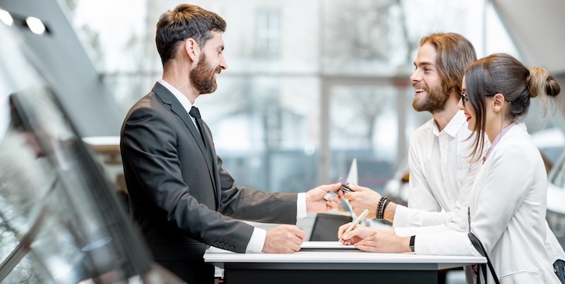 A young couple discusses buying a used vehicle with a dealership salesman.