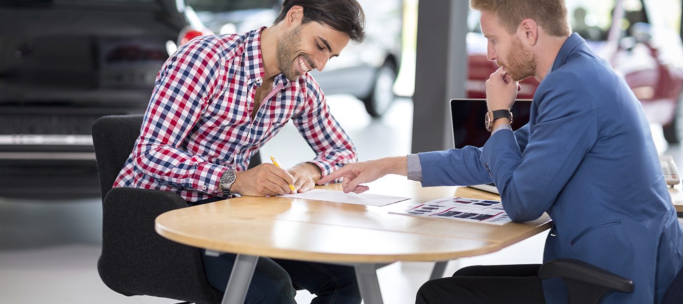 Happy man with car dealer buying a car signs the contract in car showroom